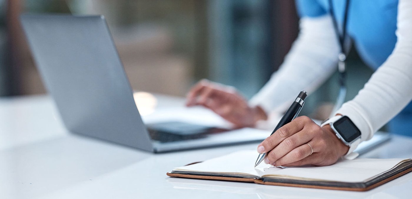 Health worker making notes while using a laptop