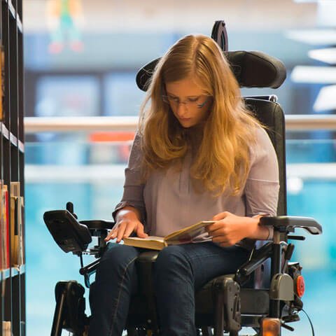 An adult female in a wheelchair in a library reading