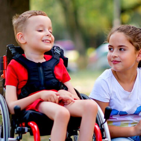 Young boy in a wheelchair outside next to a young girl