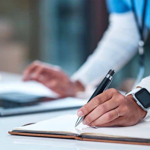 Health worker making notes while using a laptop