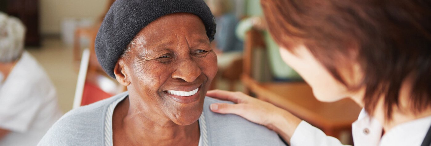 Smiling elderly women with healthcare worker resting a hand on her shoulder