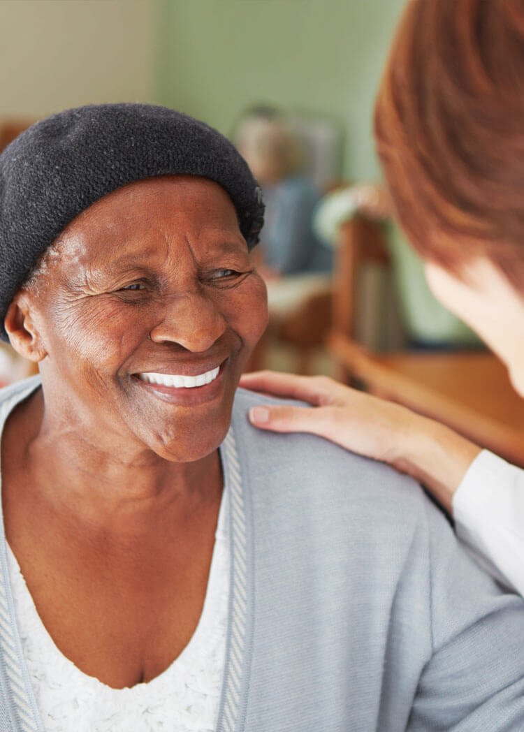Smiling elderly women with healthcare worker resting a hand on her shoulder